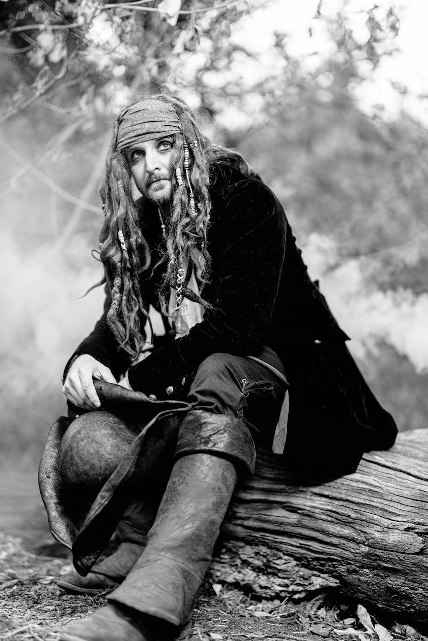grayscale shot of a man dressed as a pirate sitting on a fallen tree