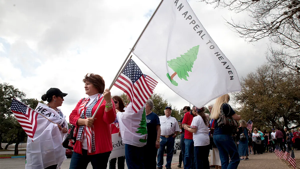 A group of Americans display the “Appeal to Heaven” flag (also known as the Pine Tree Flag) alongside U.S. flags at a public rally. This Revolutionary War-era flag has recently sparked debate after its appearance at a federal agency.